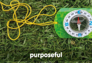 a compass with a yellow neck cord sat on a piece of grass with the word purposeful